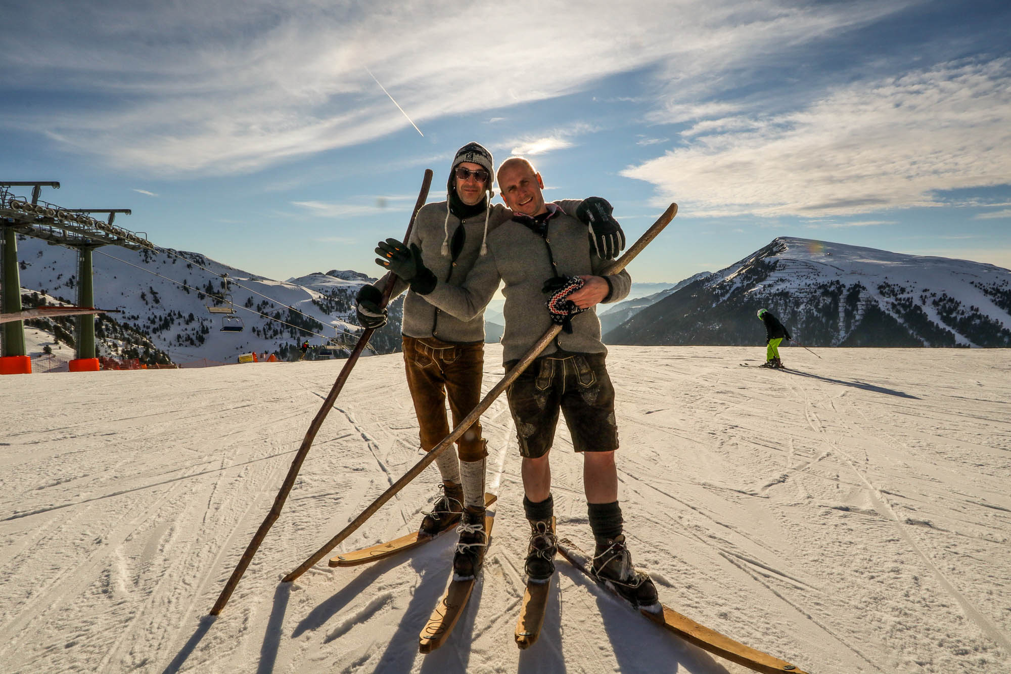 Zwei Männer in Tracht stehen vor dem Panorama in Obereggen auf historischen Ski