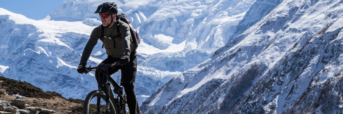 Ein Mountainbiker fährt vor einem vereisten Himalaja-Massiv