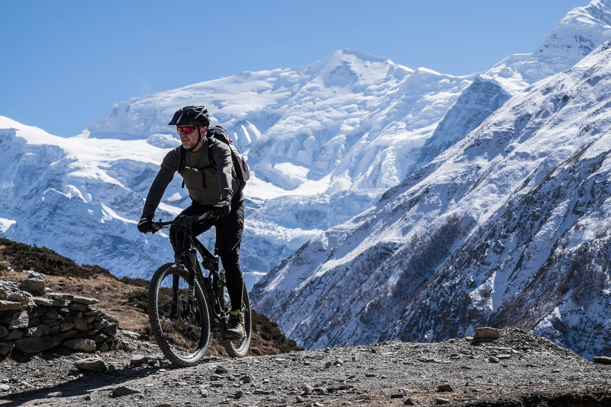 Ein Mountainbiker fährt vor einem vereisten Himalaja-Massiv